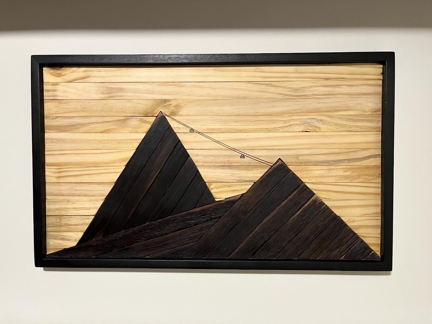 Quadro autoral em madeira representando montanhas e um teleférico.