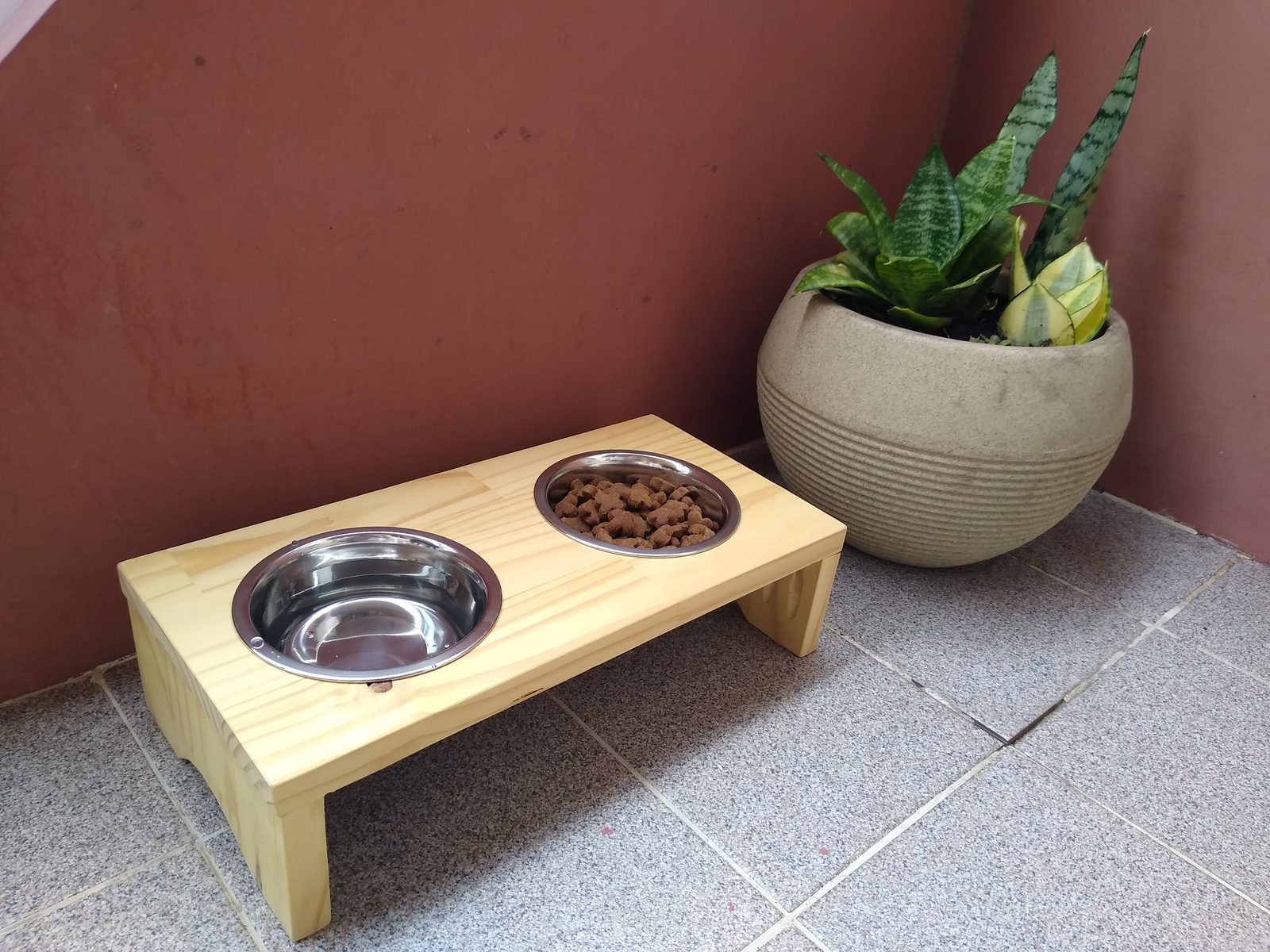 Comedouro elevado de madeira clara com dois recipientes de inox.