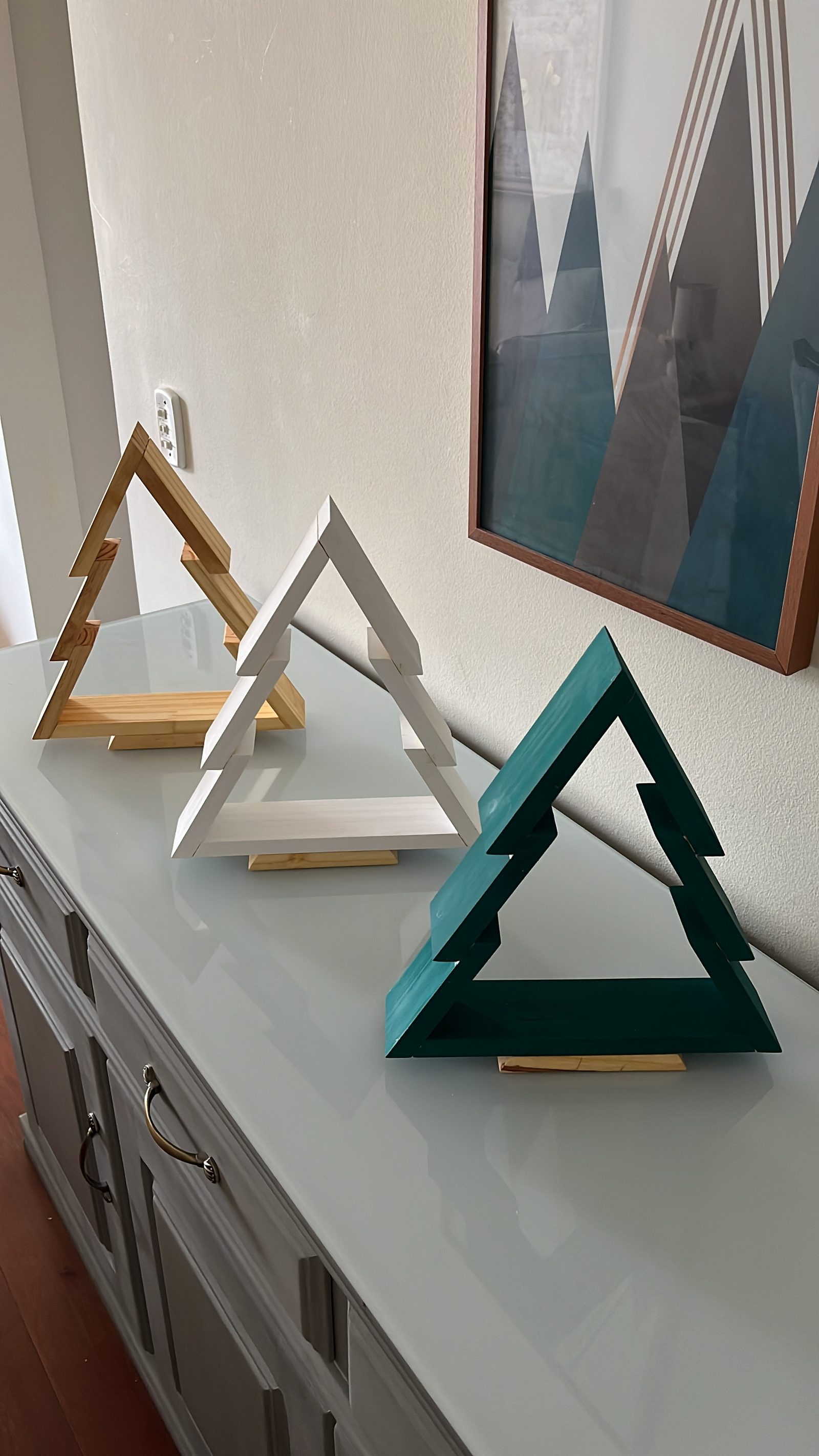 Três árvores de Natal de madeira em acabamentos natural, branco e verde.