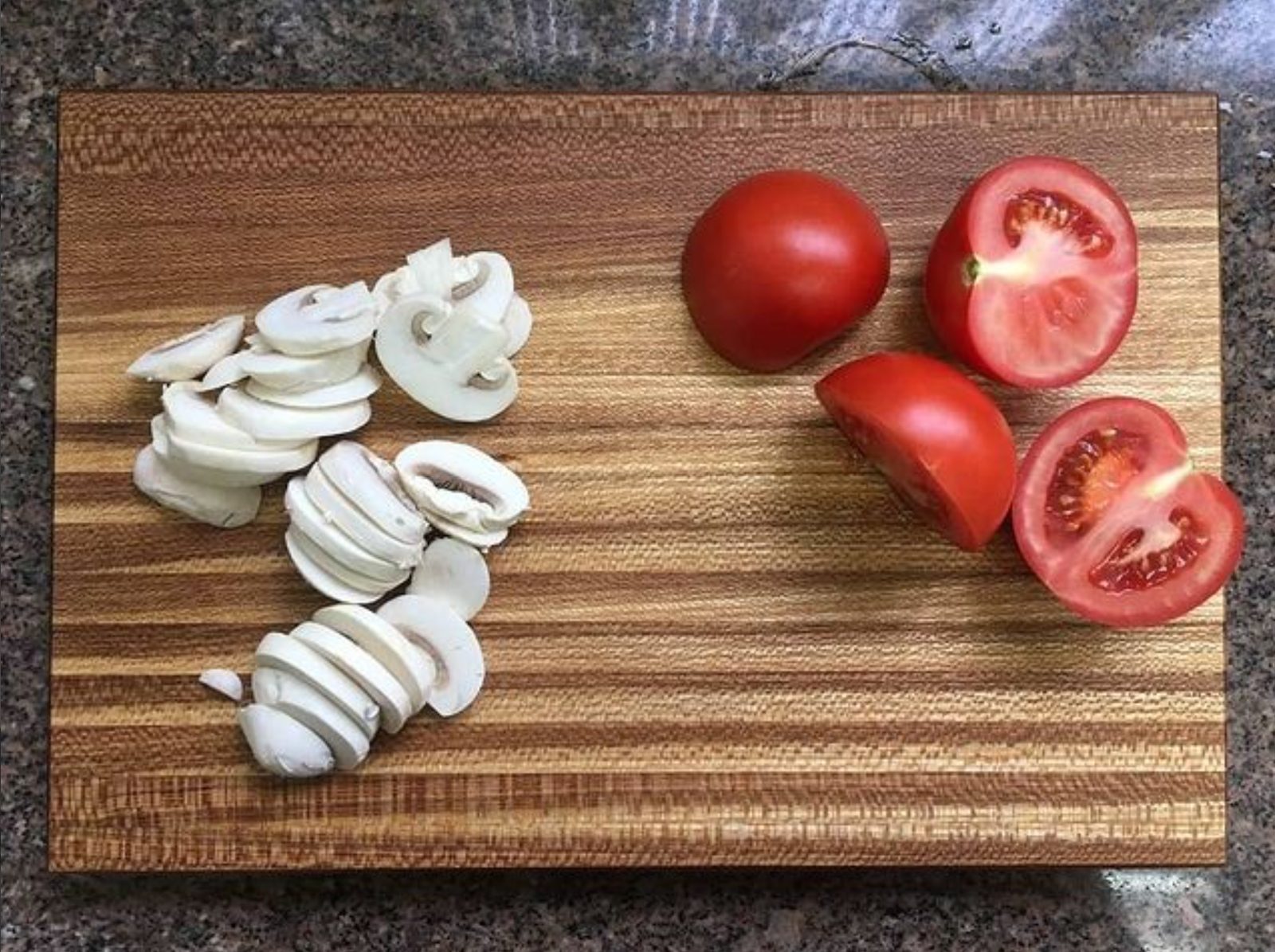 Tábua artesanal de madeira com cogumelos e tomates fatiados.
