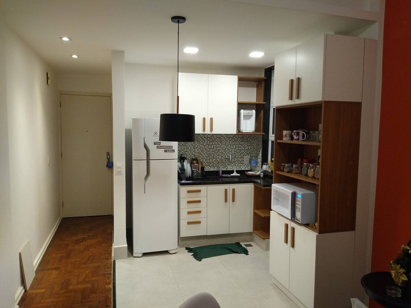 Vista ampla de cozinha compacta com armários brancos e nichos em madeira.