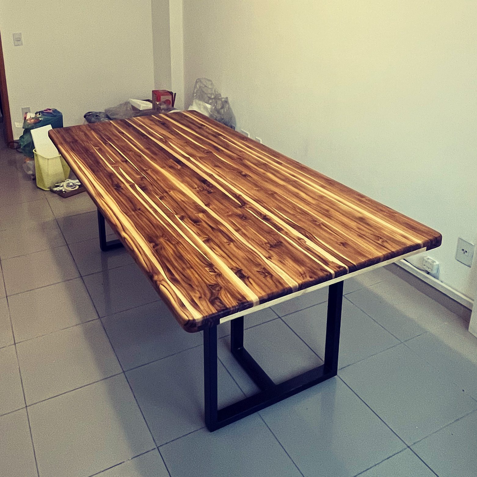 Mesa de madeira maciça com veios marcantes e base metálica preta.